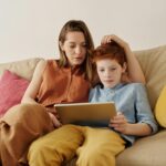 A mother and her son sitting on a couch, using a tablet for education and bonding time.
